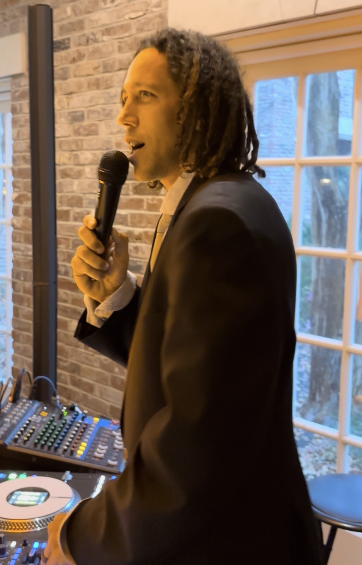 DJ Keith Anthony speaking into a microphone as MC at a wedding reception, mixer visible in the background