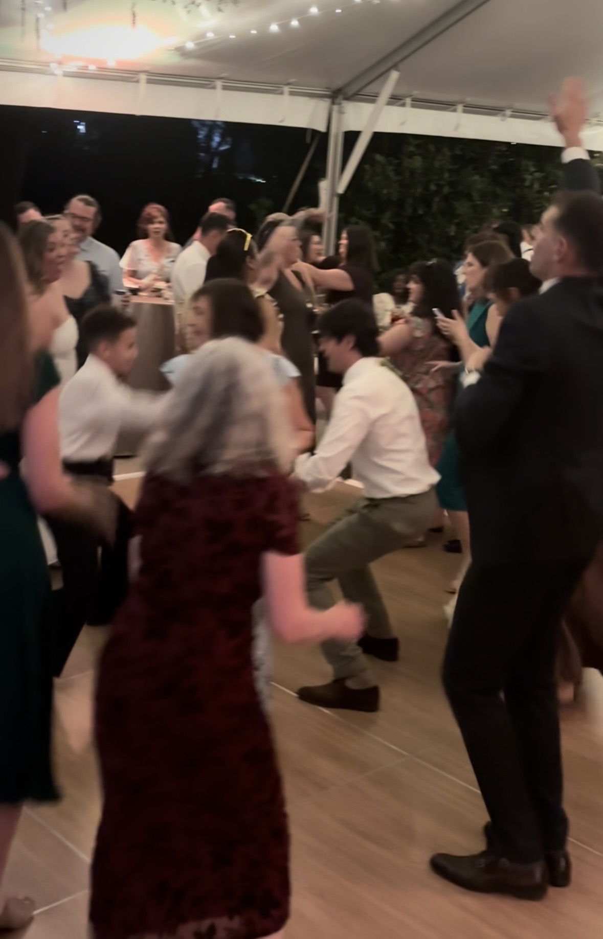 Wedding guests dancing together on a packed reception dance floor under a tent